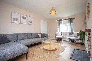A living room with a grey sofa, a round coffee table, a chair, a small table, and a plant.