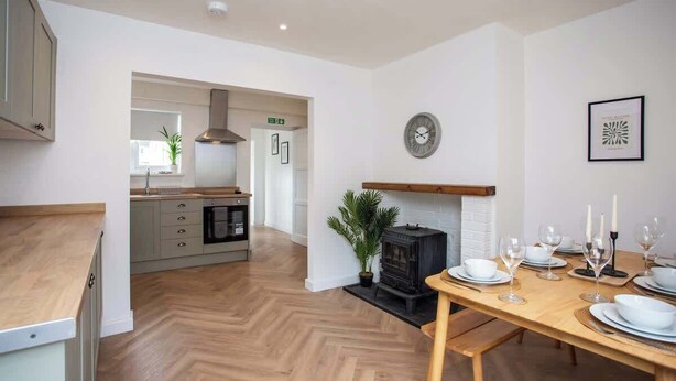 A modern kitchen with a dining area, wooden flooring, a built-in stove, and a clock on the wall. - Vacant Nest | The South End | Spacious | Smart TV (Kielder)