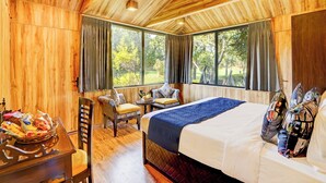 A wooden-paneled room with a bed, a chair, a small table, and a window with curtains. - Alaya Stays Fortezza | Pet-friendly 6-BHK Farmhouse With Private Pool (Sohna)
