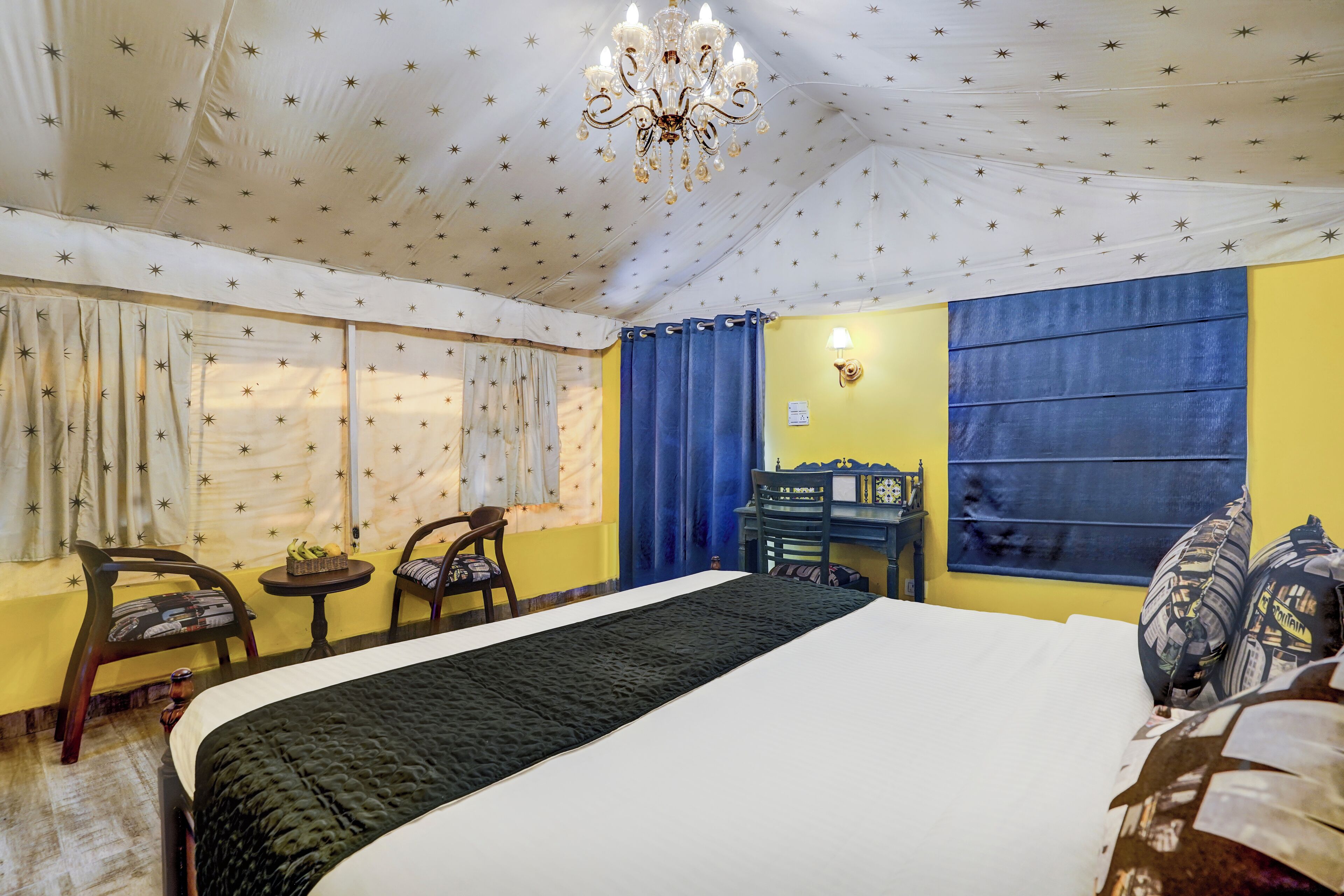 A hotel room with a bed, two chairs, a small table, a desk, and a chandelier.