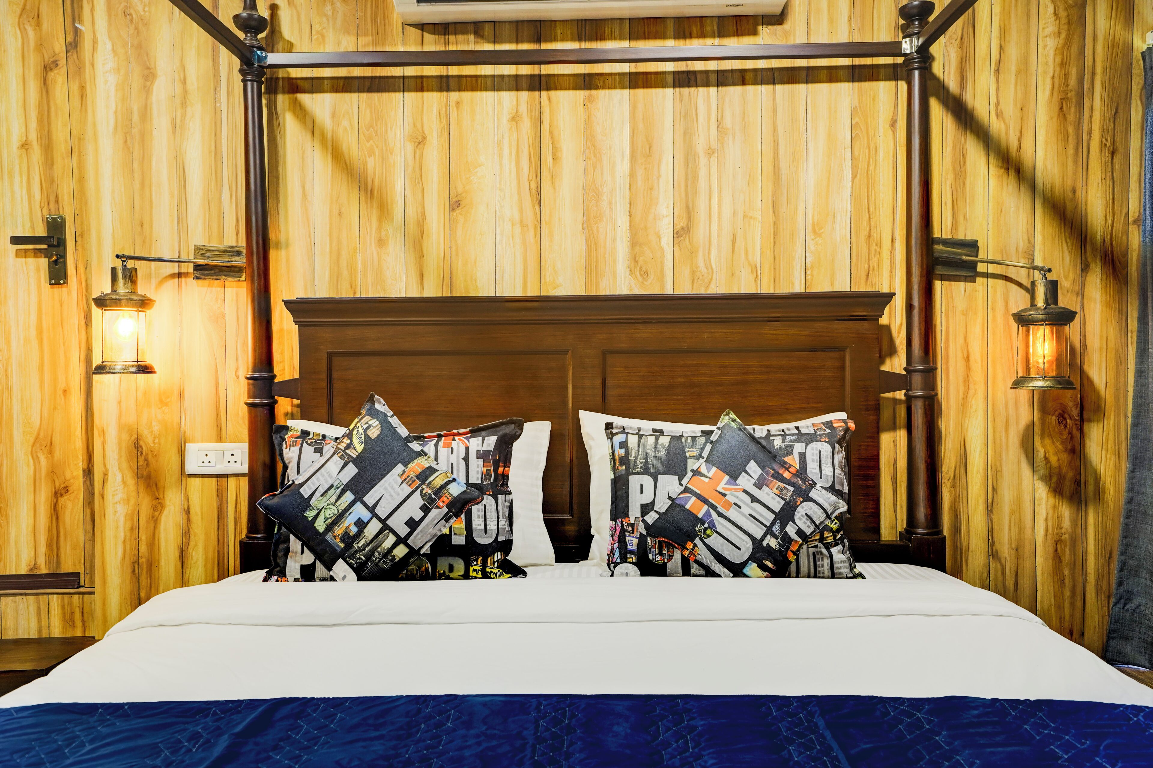 A wooden-paneled room with a four-poster bed, two decorative pillows, and wall-mounted reading lamps.