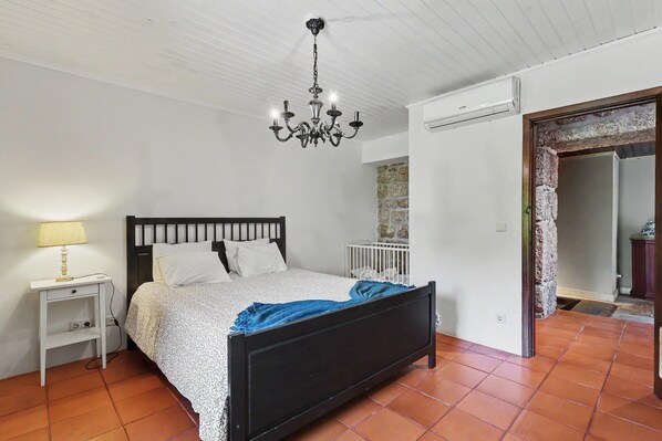 A bedroom with a bed, a nightstand, a chandelier, a crib, and a stone wall.