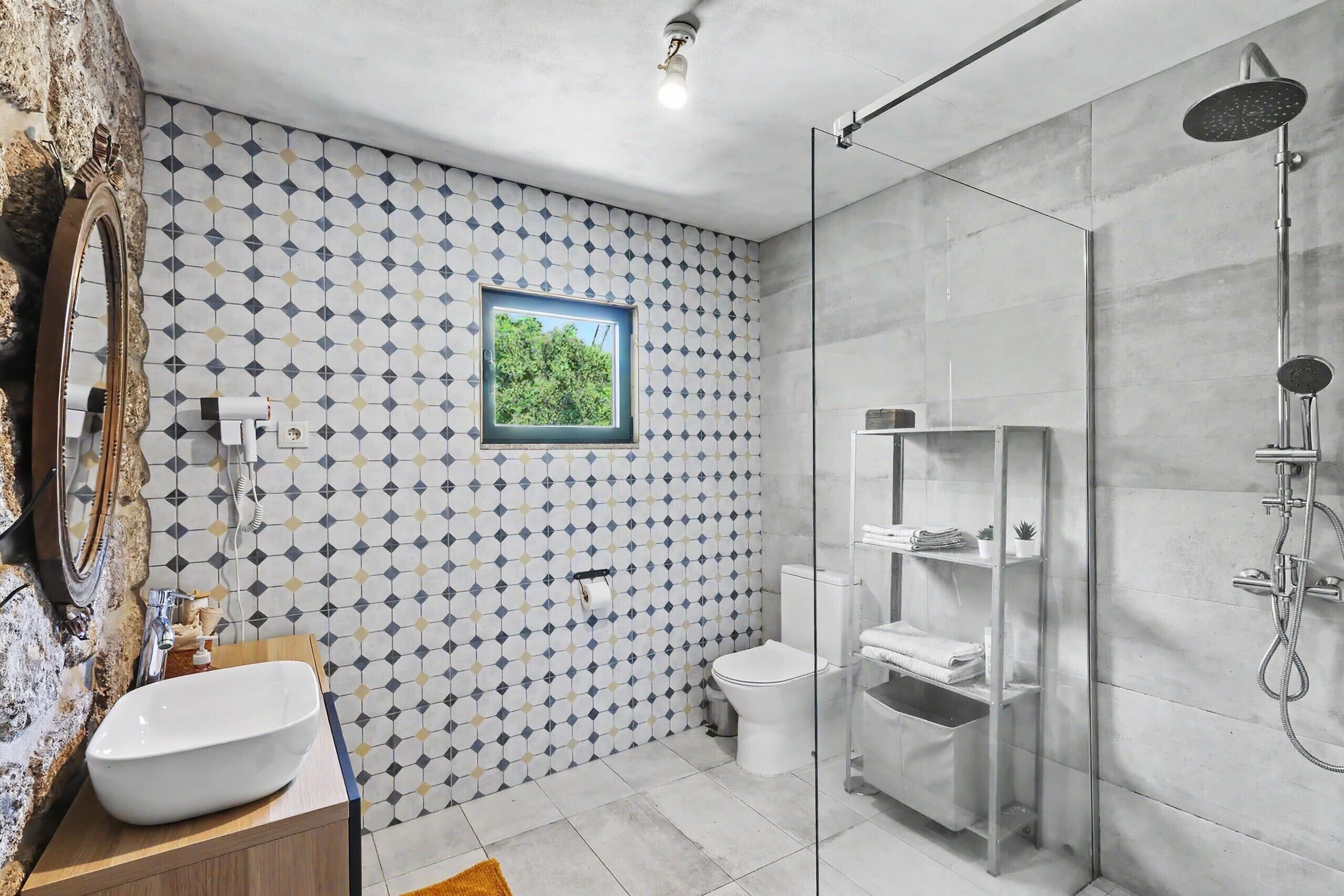 Un bagno moderno con pannelli di piastrelle geometriche, uno specchio grande, un lavandino, un water e una cabina doccia in vetro.