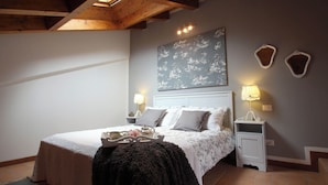 A bedroom with a bed, two bedside tables, a nightstand, a wall-mounted lamp, and a decorative wall piece. - Snug Nest (Como)