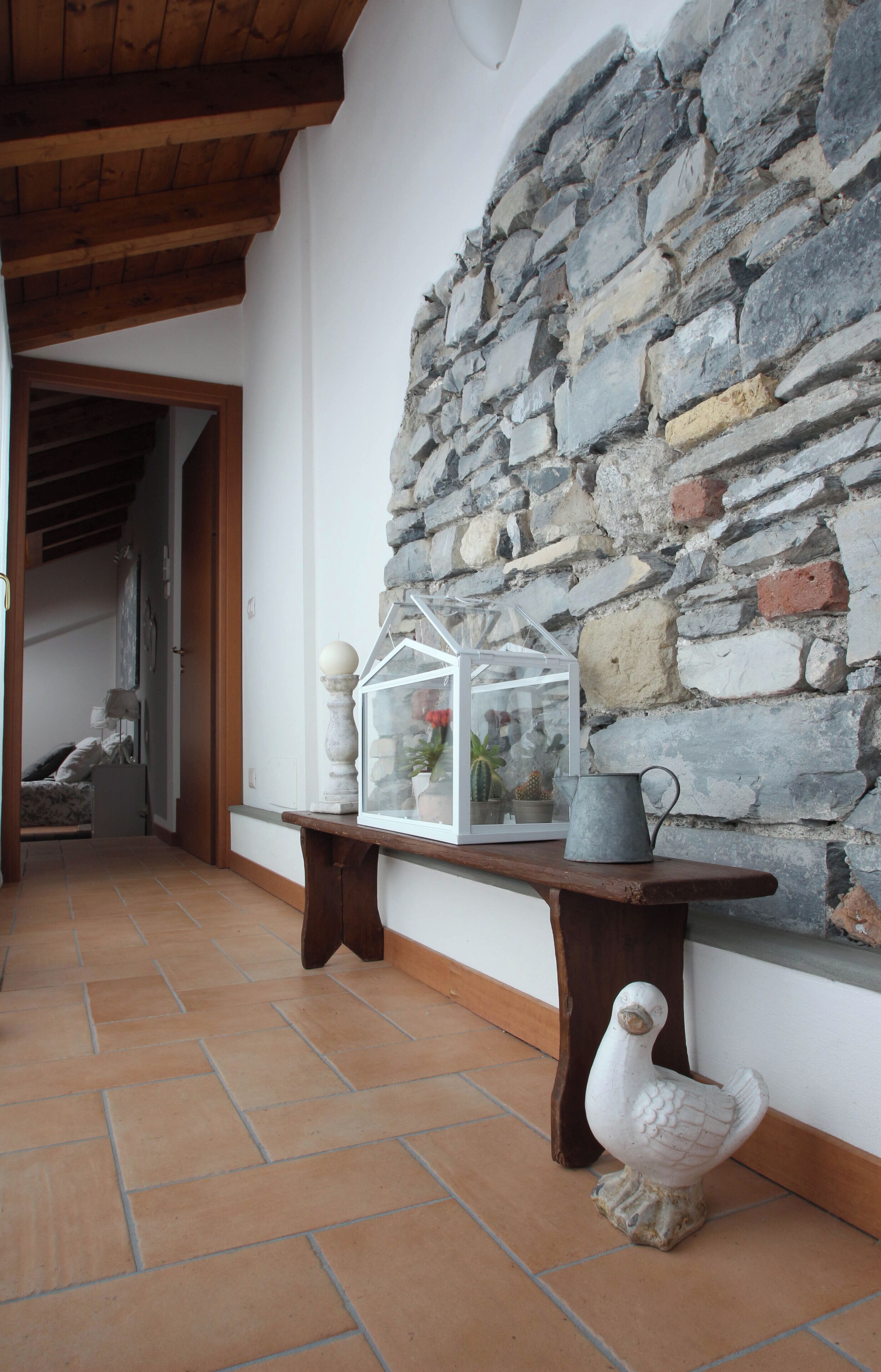 A hallway with a stone wall, a wooden bench, a glass house, and a ceramic rooster.