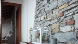 A hallway with a stone wall, a wooden bench, a glass house, and a ceramic rooster. - Snug Nest (Como)