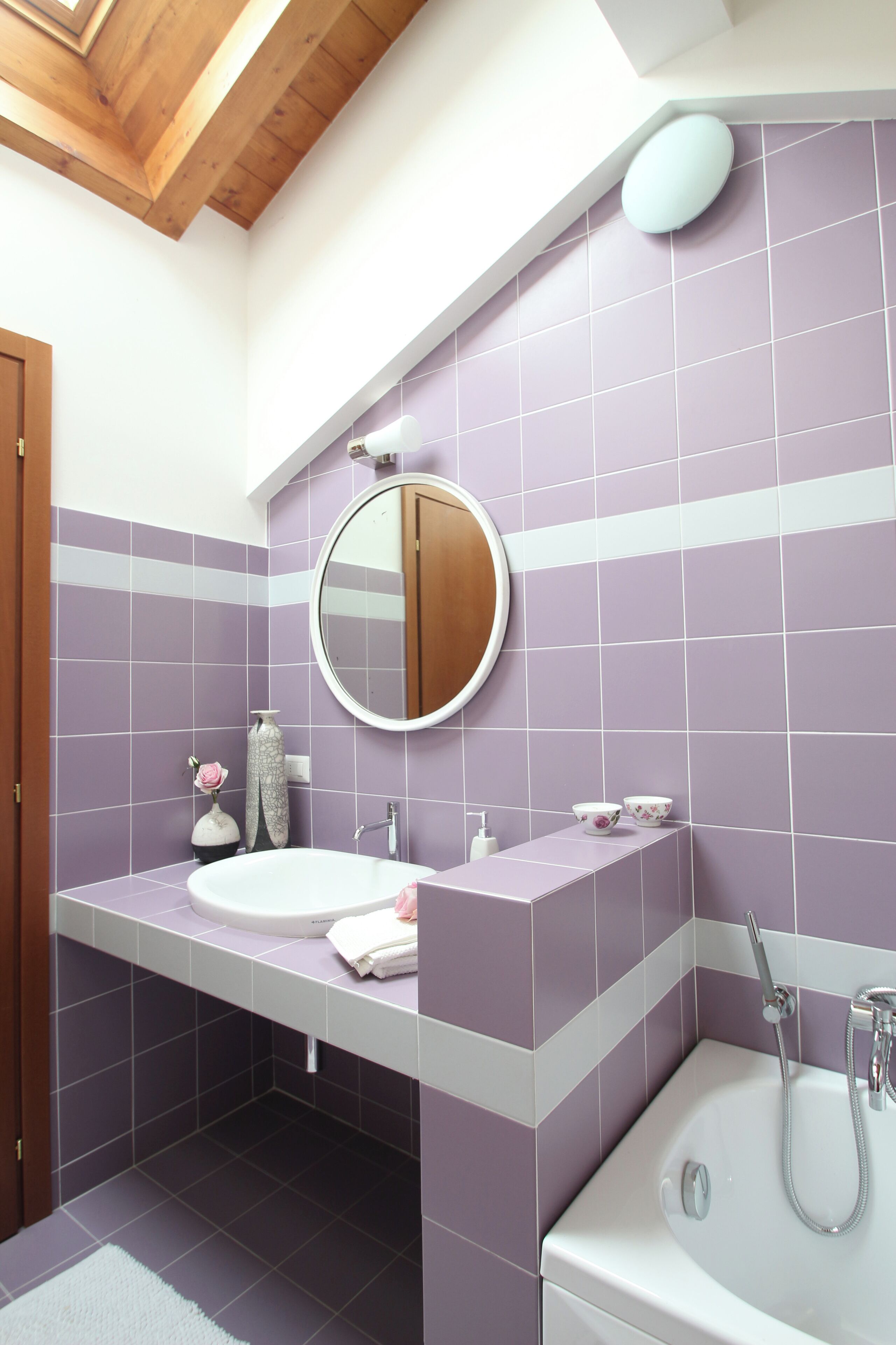 A bathroom with a white sink, a round mirror, and a bathtub.