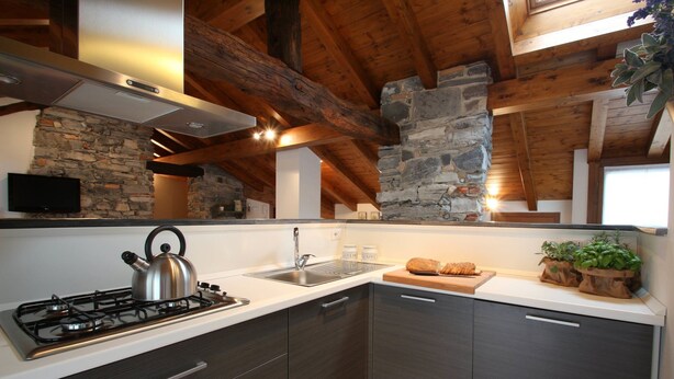 A modern kitchen with a gas stove, a sink, and dark wooden cabinets. - Snug Nest (Como)