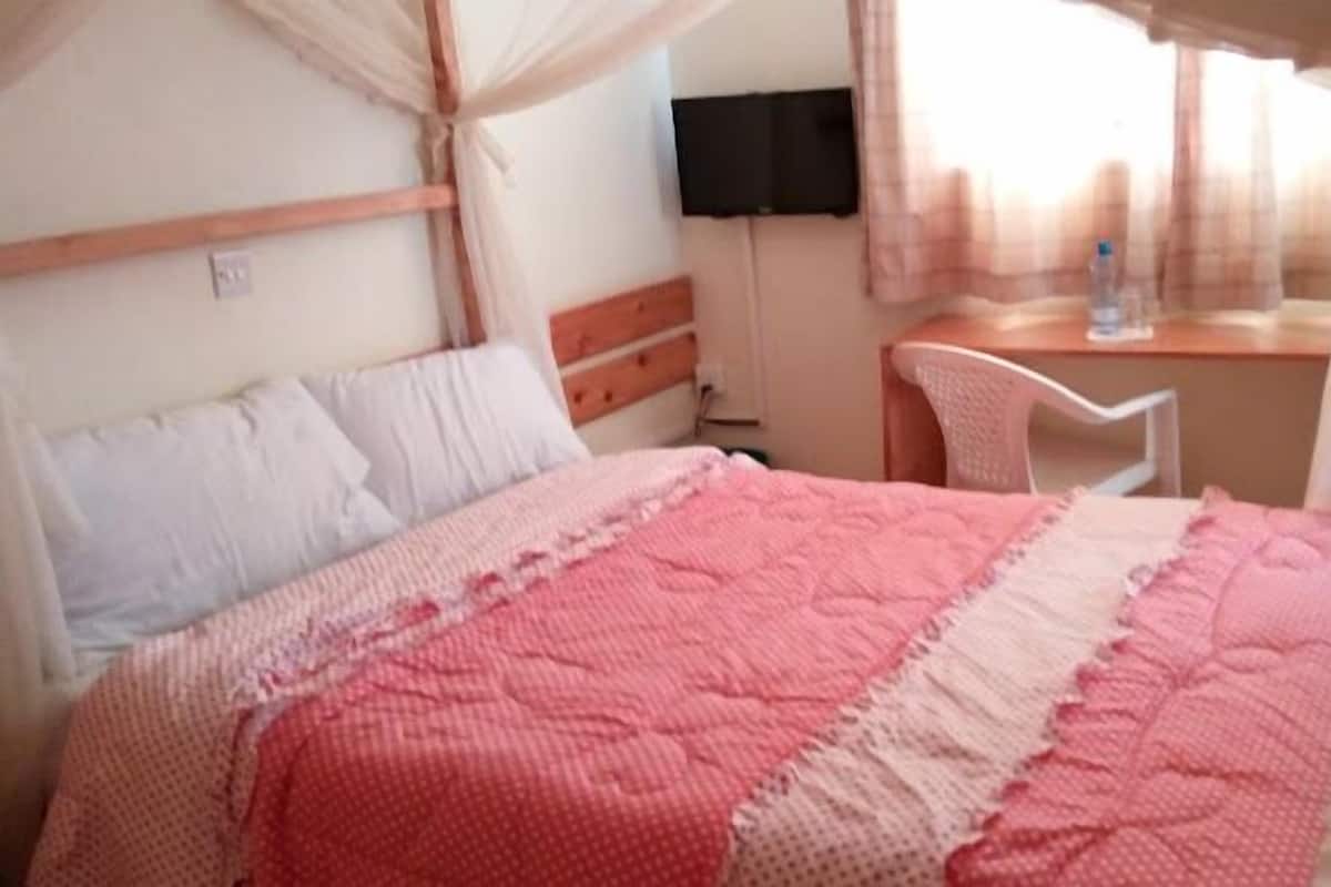 A bedroom with a bed, a desk, a chair, and a television.