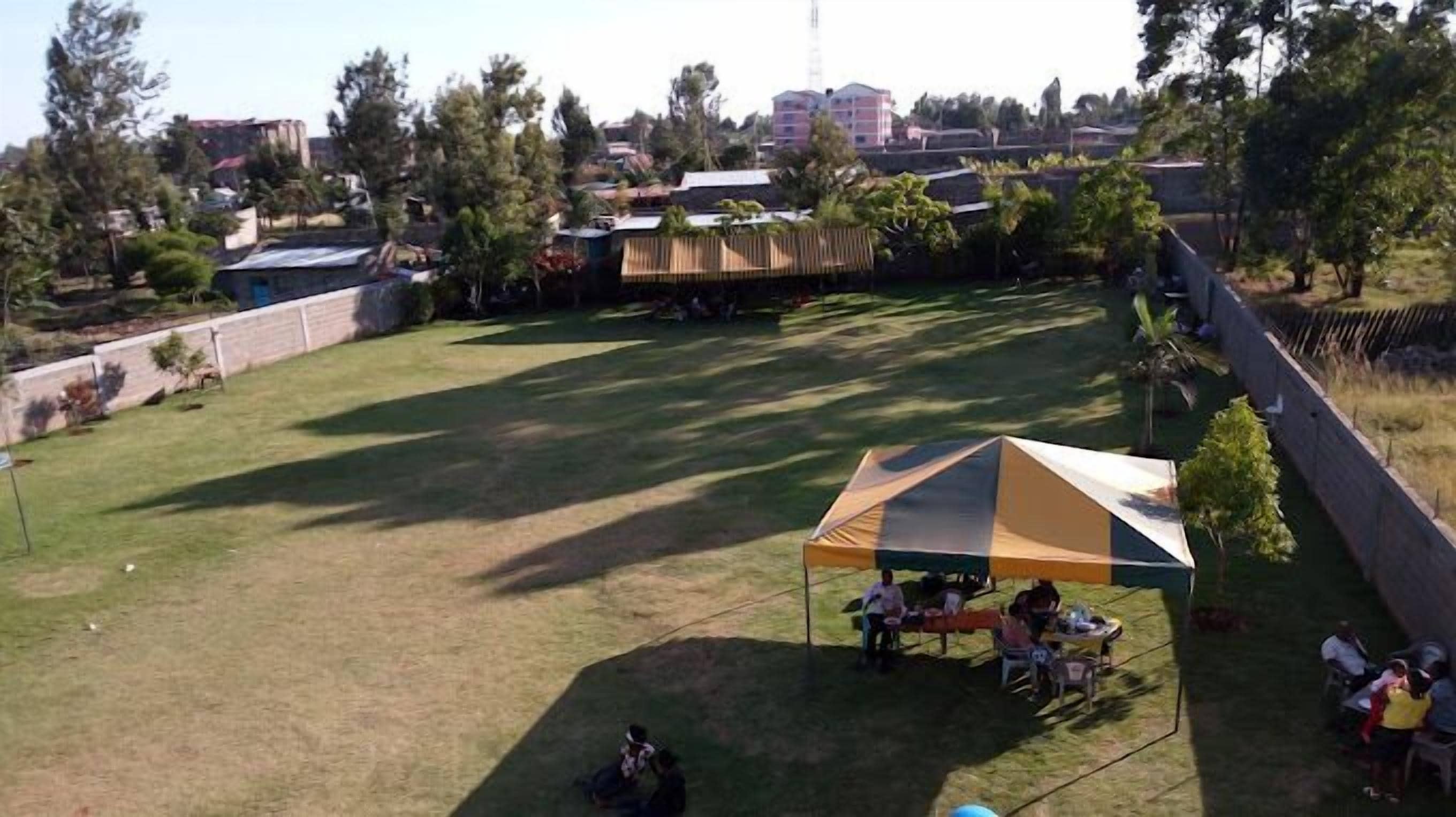 An outdoor area with a grassy field, a tent, and a few people gathered around.