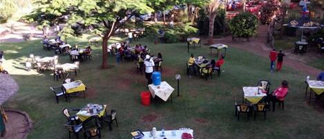 An outdoor dining area with tables and chairs arranged under trees.