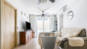 A living room with a sofa, a TV on a wooden cabinet, a ceiling fan, and a view through a glass door. - A&N Yecla Torre del Mar (Torre del Mar)