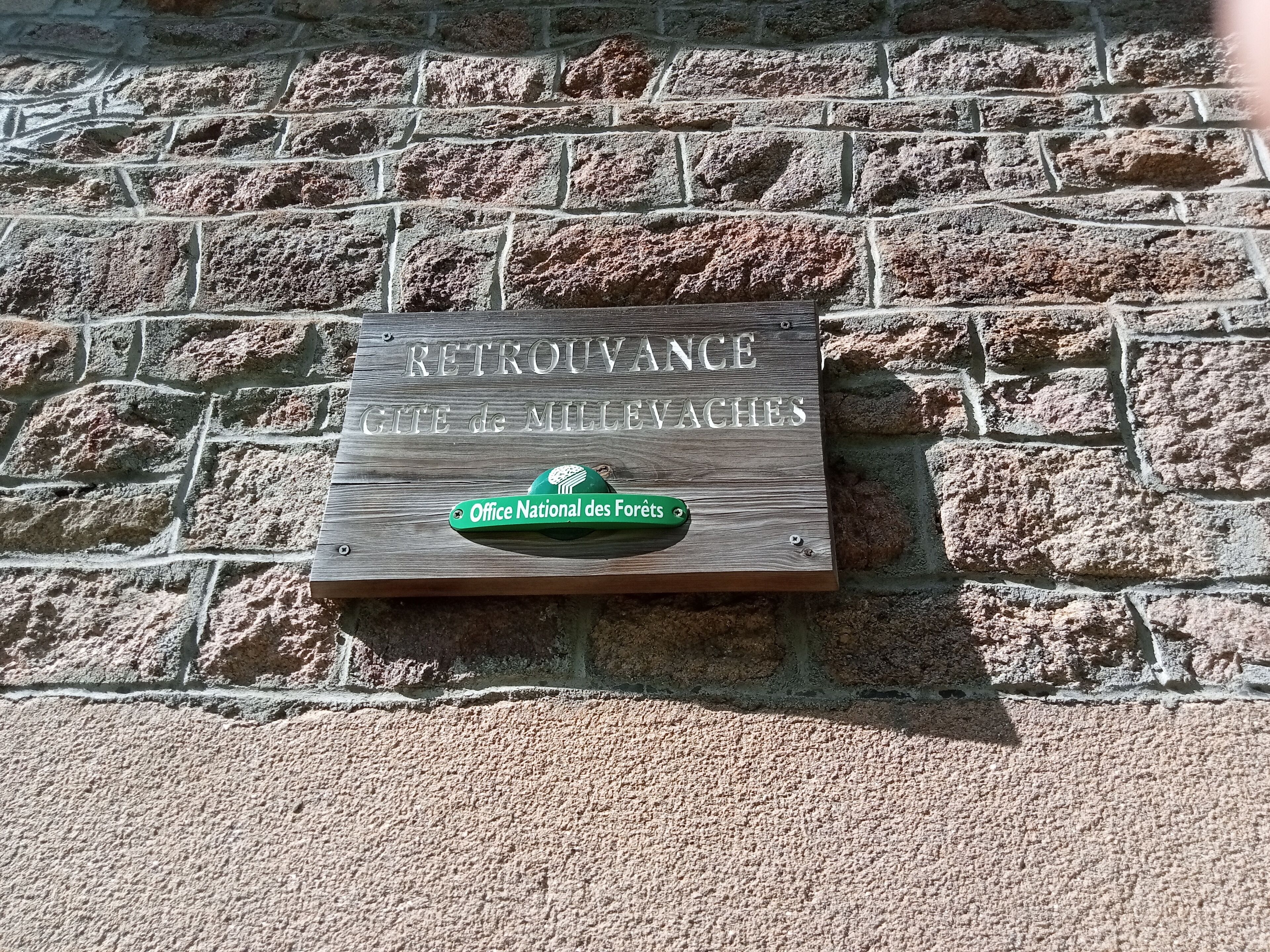 Eine Tafel an einer Steinsäule mit dem Text 'RETOURVANCE GITE de MILLEVACHES' und ein grüne Schild darunter.