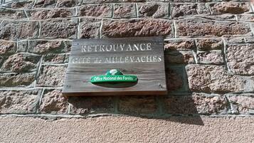 Eine Tafel an einer Steinsäule mit dem Text 'RETOURVANCE GITE de MILLEVACHES' und ein grüne Schild darunter.