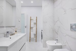 A modern bathroom with a white marble wall, a sink, a bidet, and a towel rack. - Matosinhos Coastal Studio (Matosinhos)