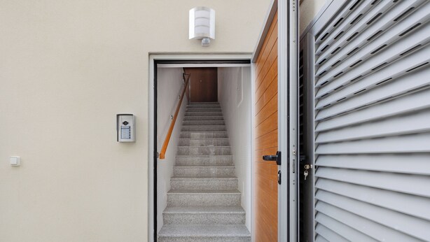 A narrow stairway leading to a wooden door, with a light fixture above and a security camera on the wall. - Matosinhos Coastal Studio (Matosinhos)