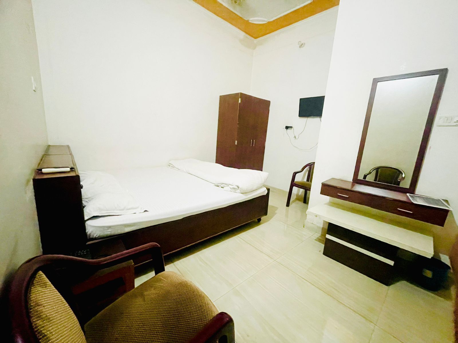 A bedroom with a bed, a wardrobe, a chair, a desk, and a mirror.