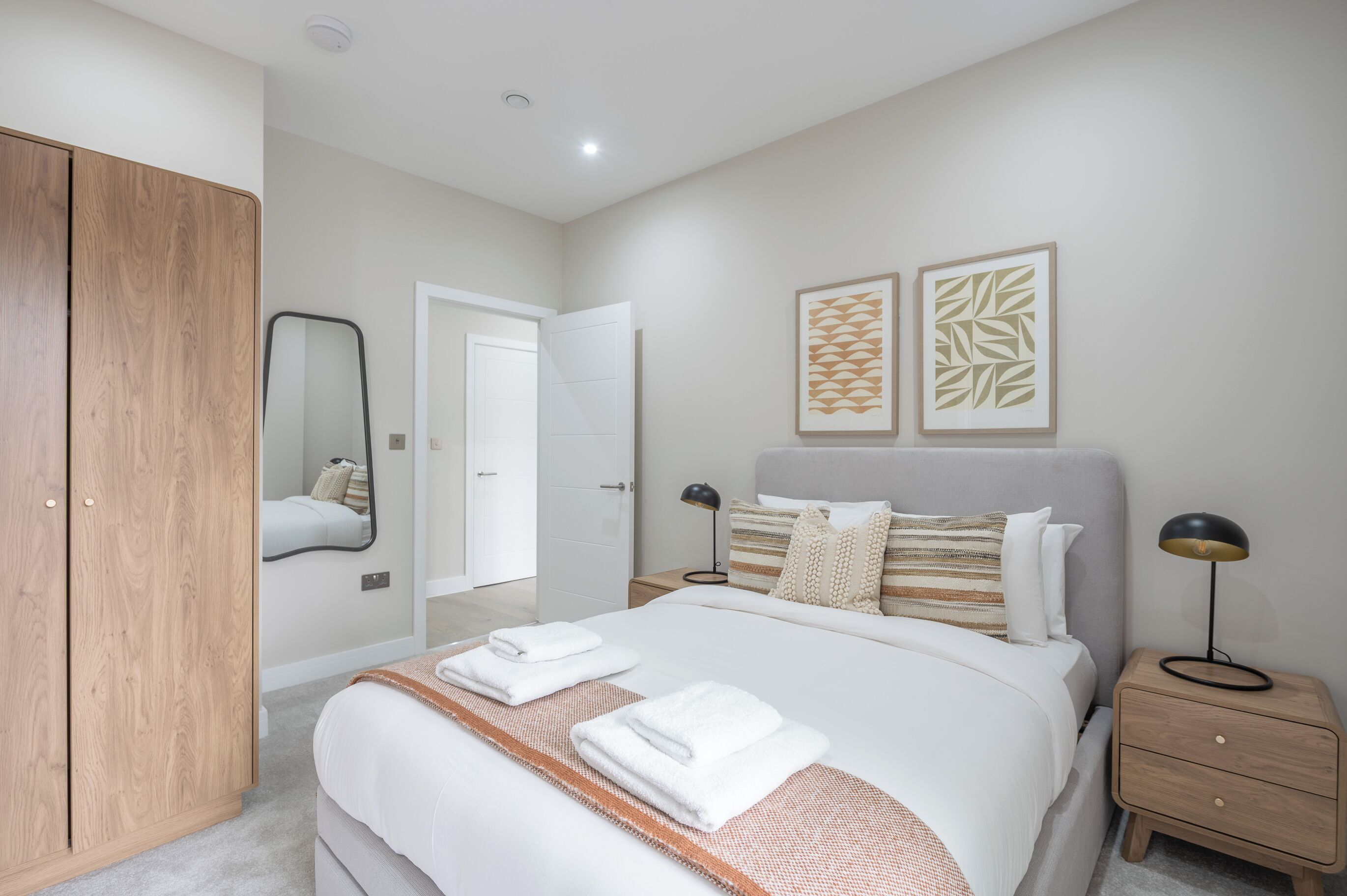 A modern bedroom with a large bed, wooden wardrobe, bedside tables, and artwork on the walls.