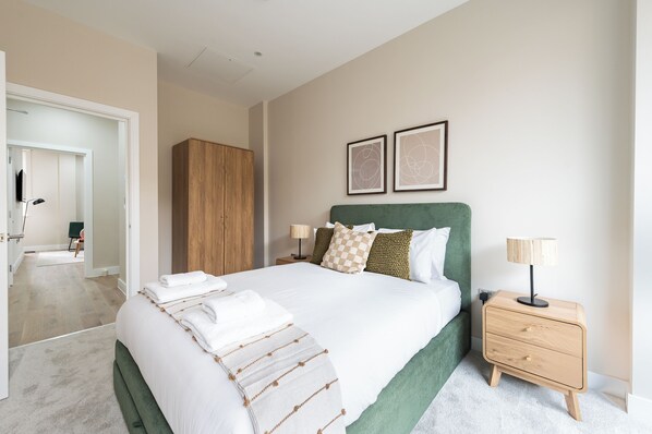 A neatly arranged bedroom with a large bed, bedside tables, a wardrobe, and two framed pictures on the wall.