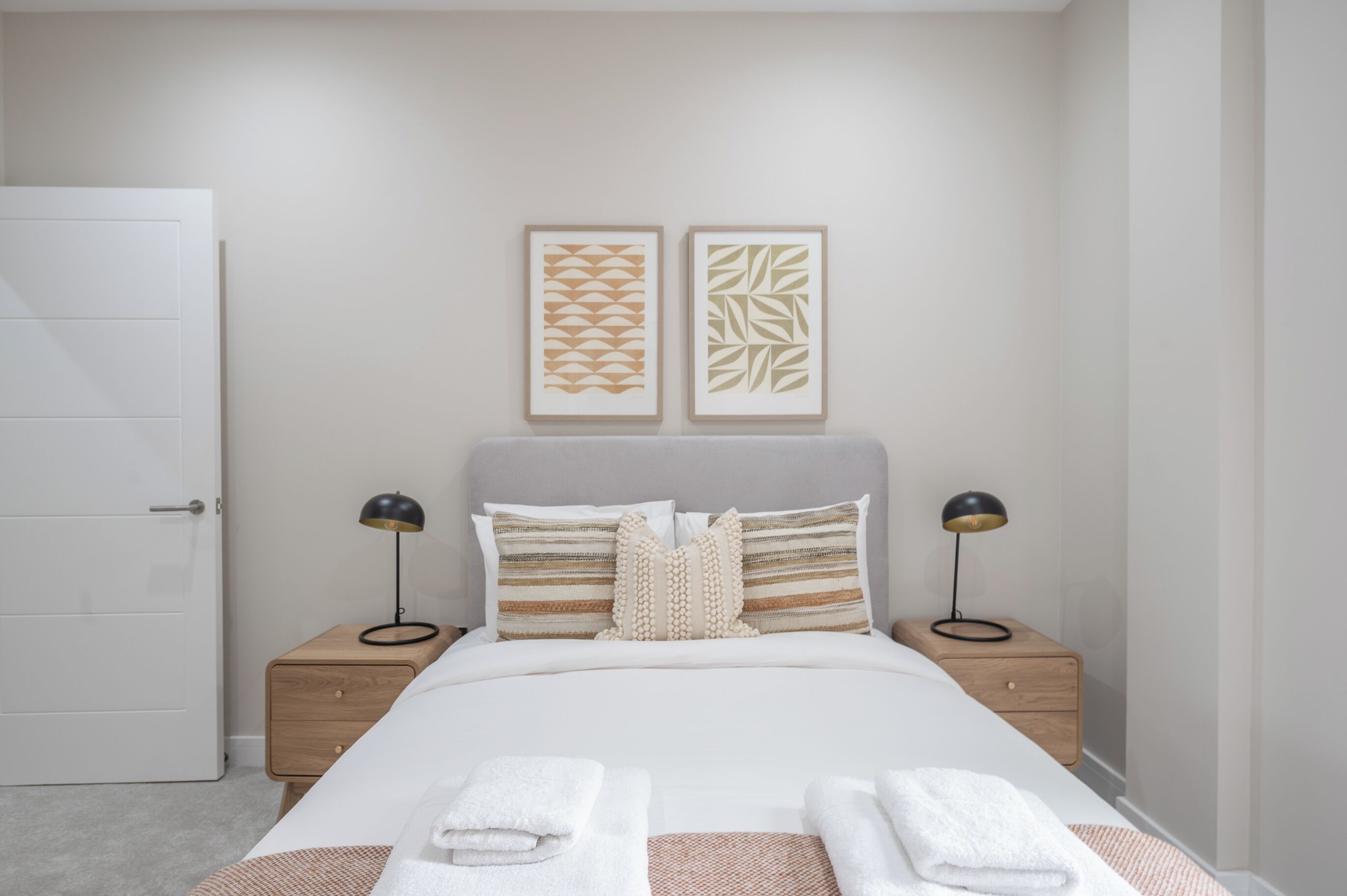A neatly arranged bedroom with a bed, two bedside tables, and two wall-mounted picture frames.