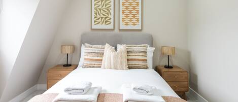Quarto bem arrumado com uma cama, duas mesas de cabeceira e duas luminárias de parede.