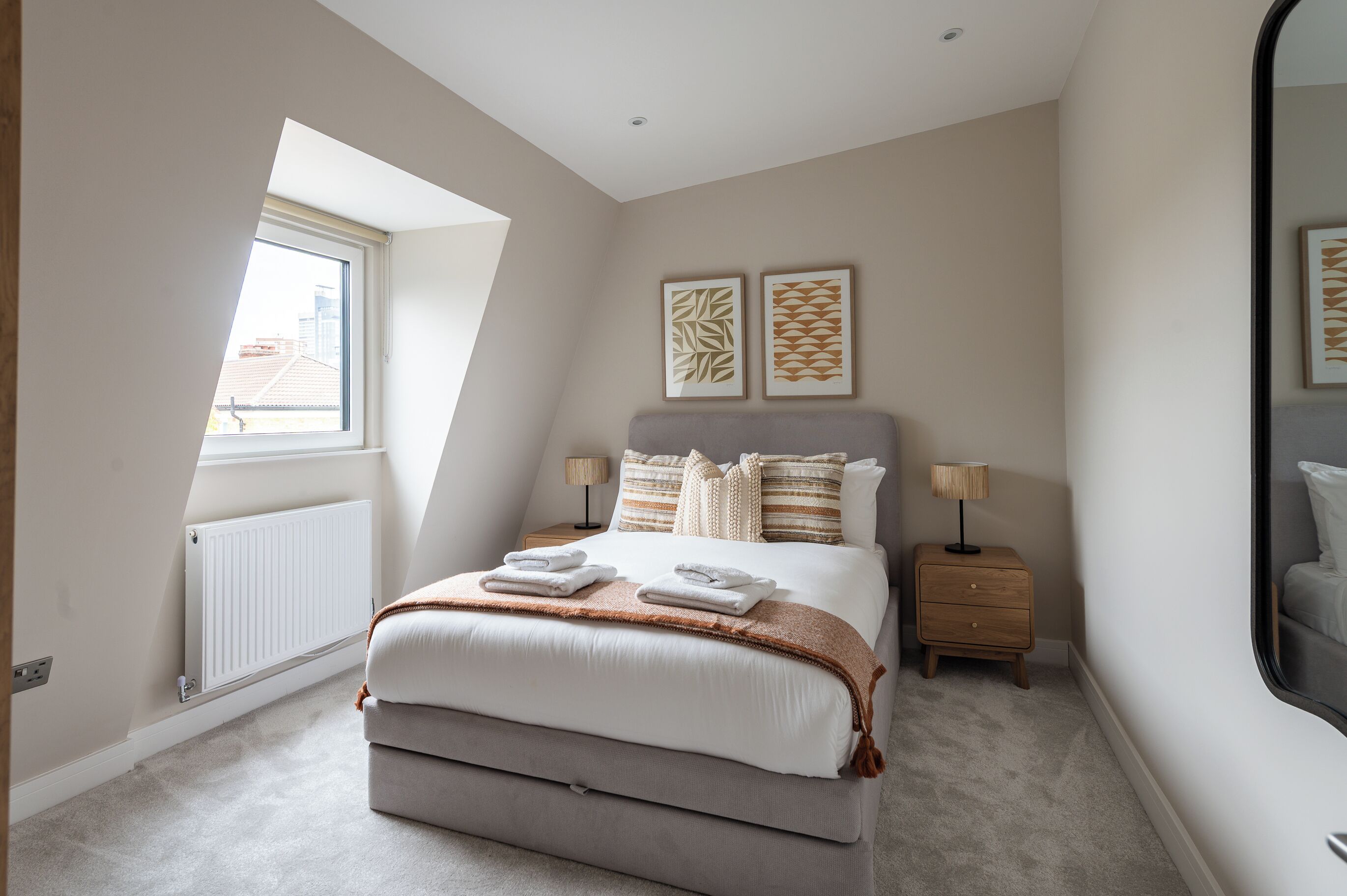 Una camera da letto con un letto, comodini, una finestra e due opere d'arte appese al muro.