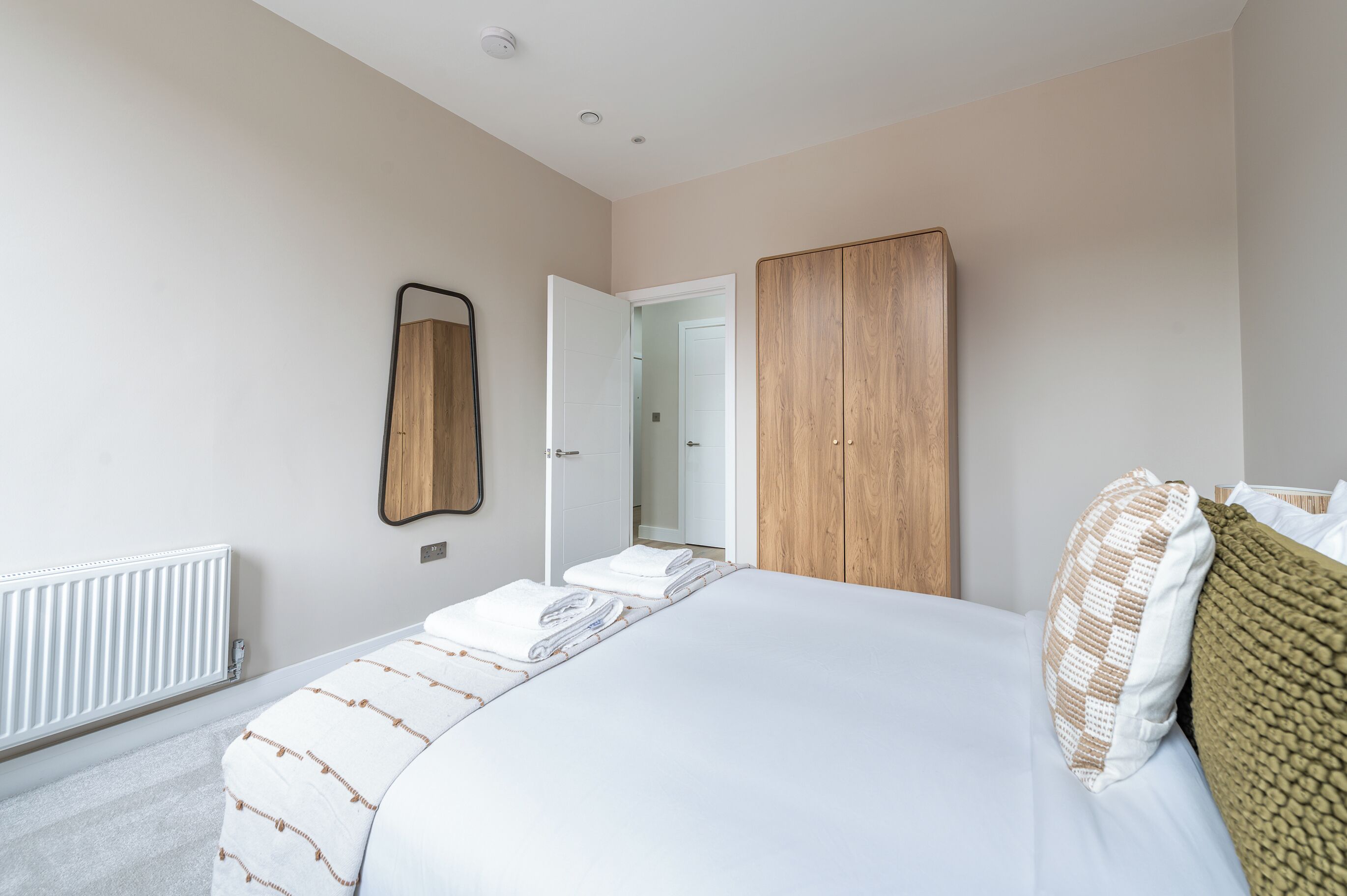 A bedroom with a bed, a wooden wardrobe, a mirror, and a radiator.