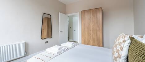 A bedroom with a bed, a wooden wardrobe, a mirror, and a radiator.