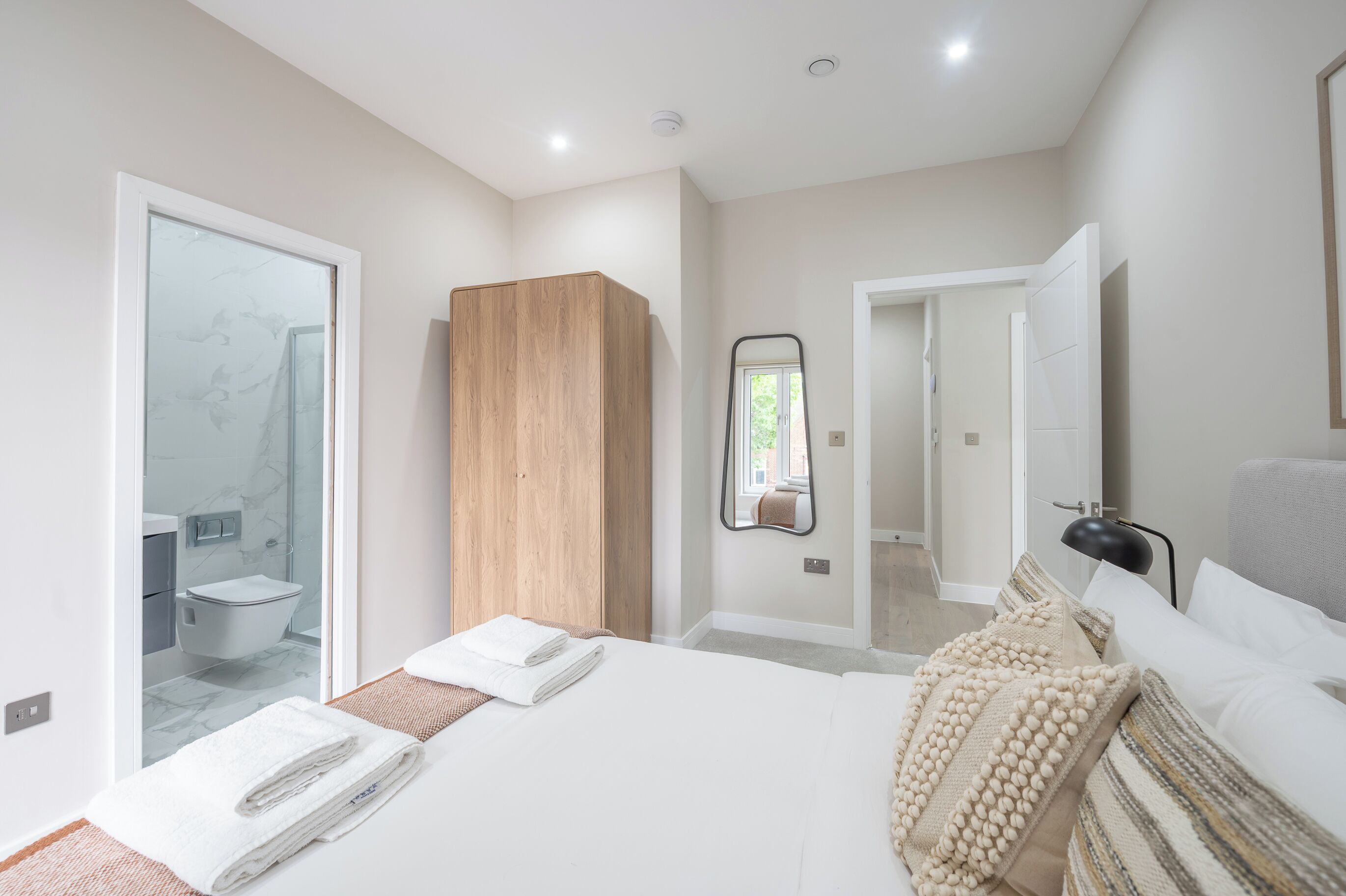 A modern bedroom with a large bed, a wooden wardrobe, a bathroom with a glass shower, and a mirror on the wall.