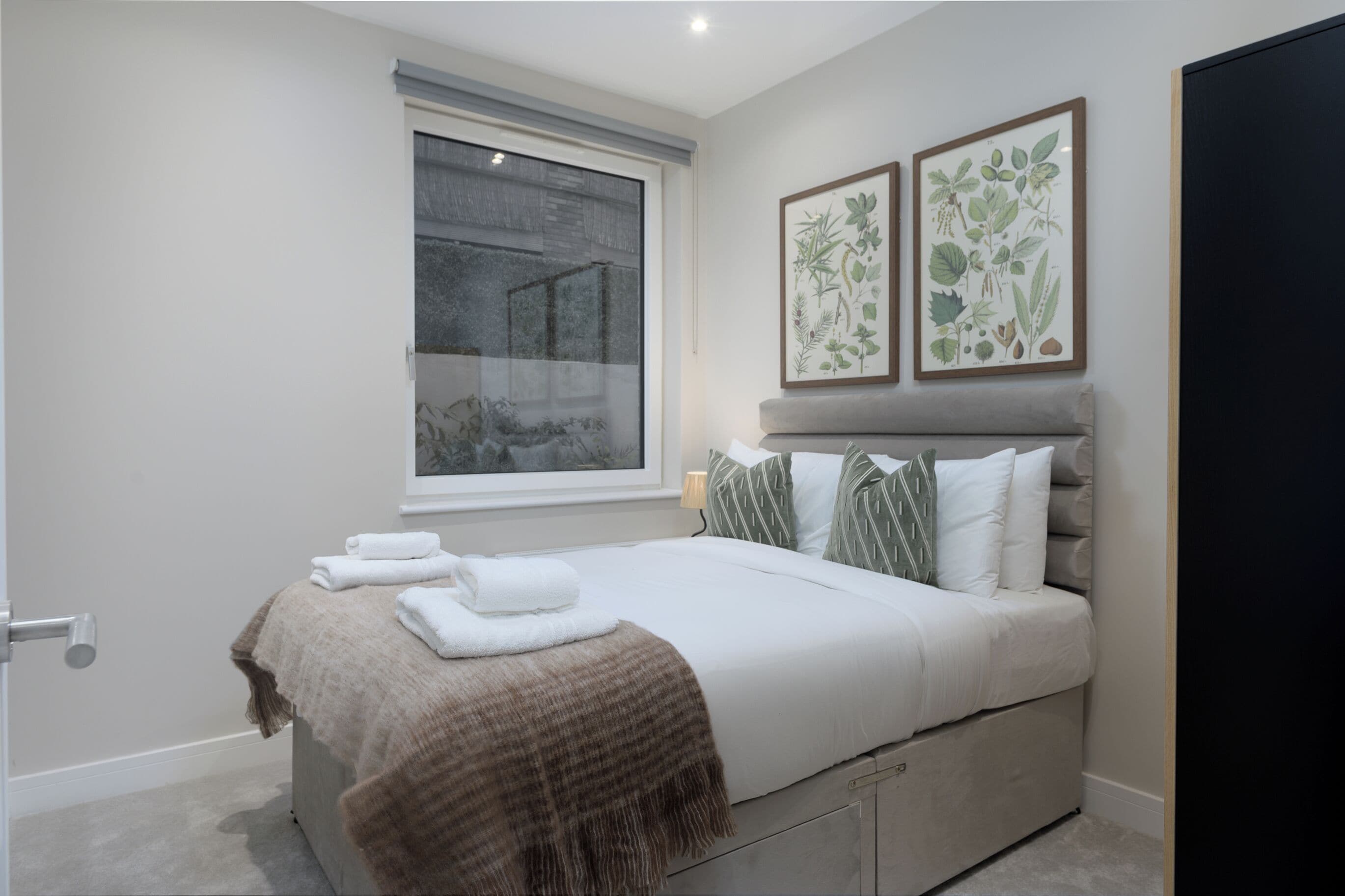 Quarto com uma cama, janela e duas gravuras botânicas emolduradas na parede.