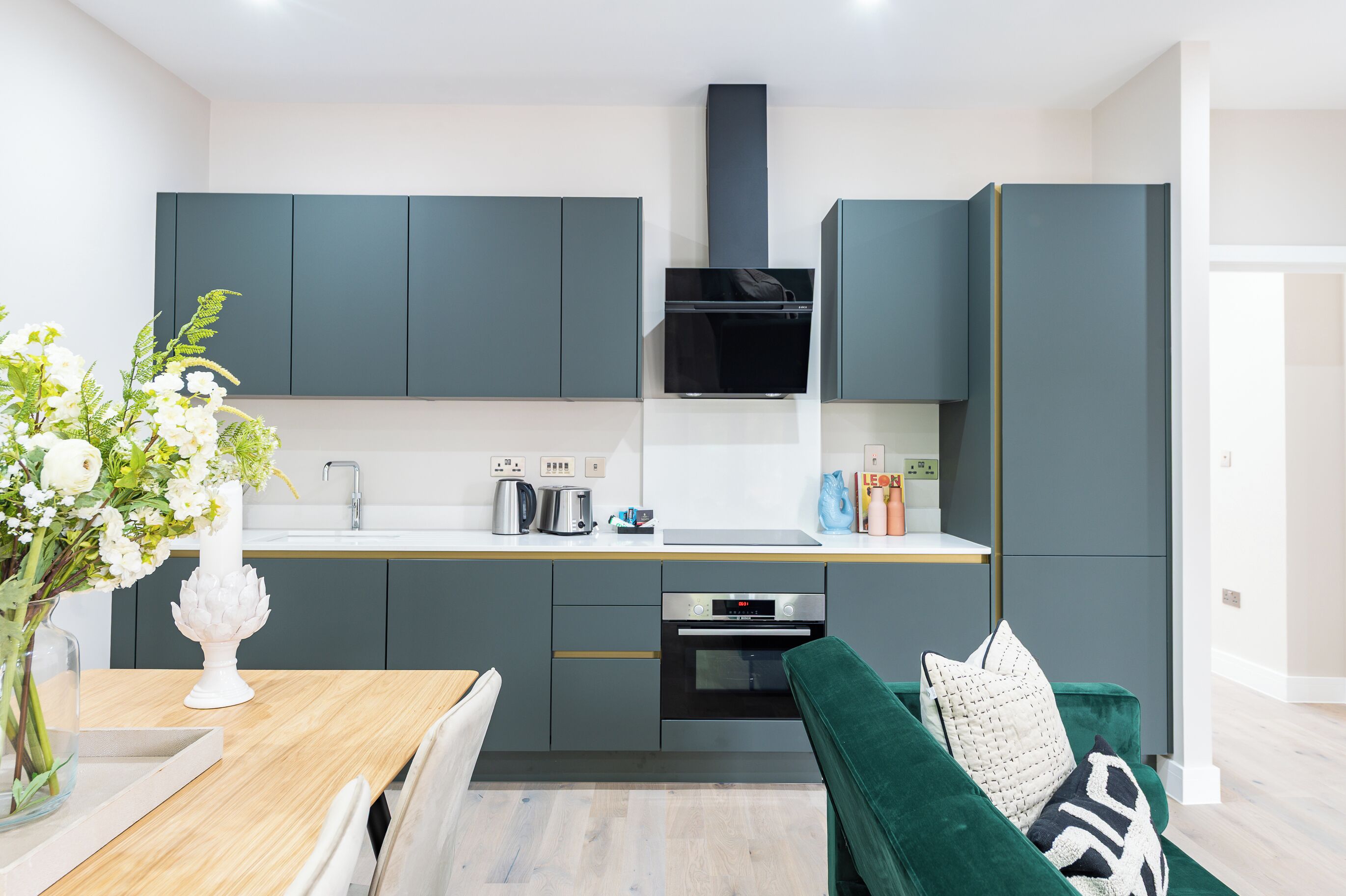 A modern kitchen with grey cabinets, a black range hood, and a built-in oven.