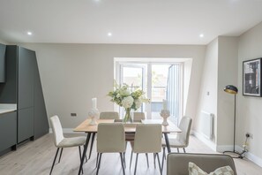 A dining area with a table, chairs, a vase of flowers, and a view through a window.