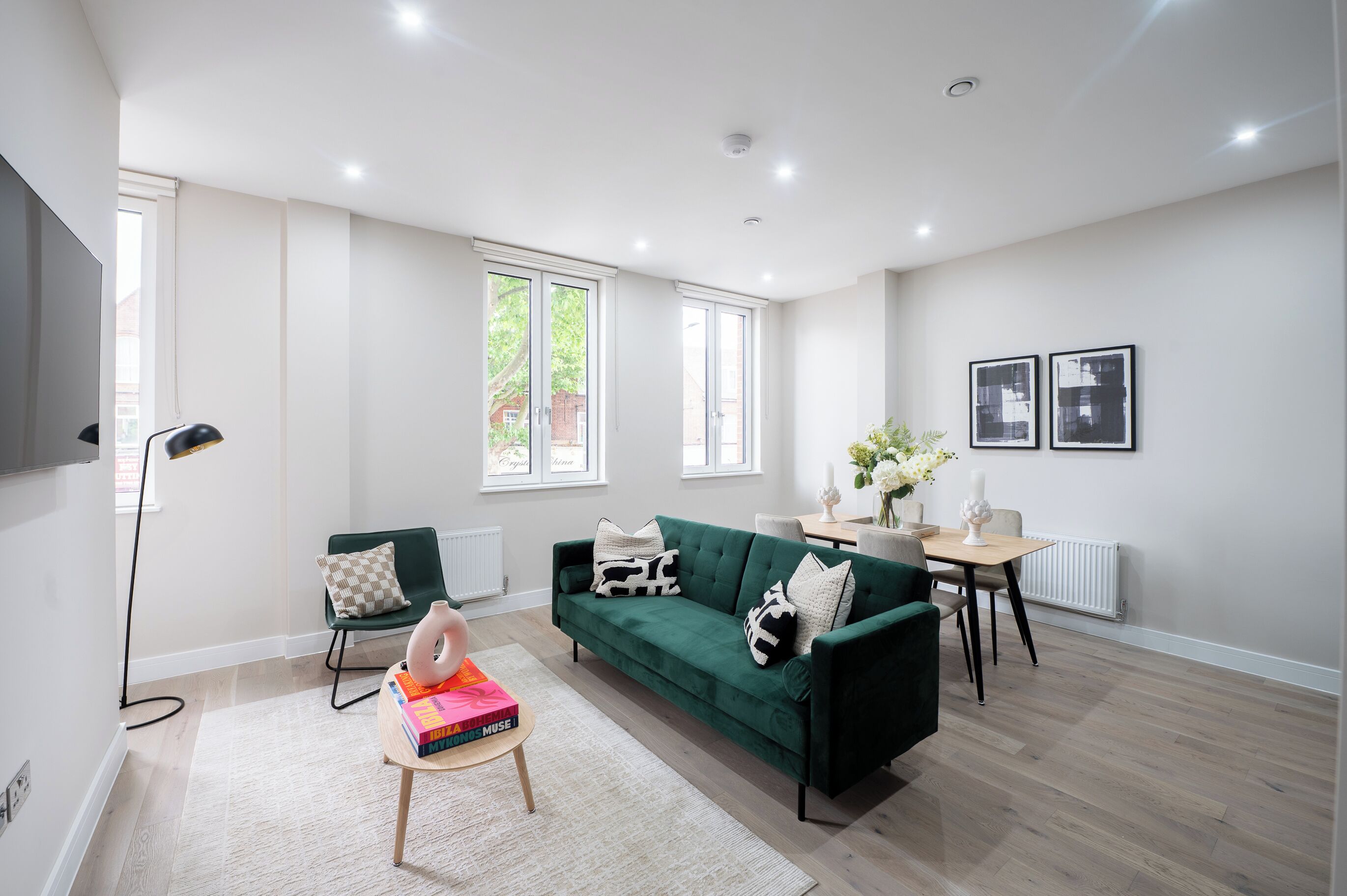 A modern living room with a green sofa, a dining table, and a bookshelf.