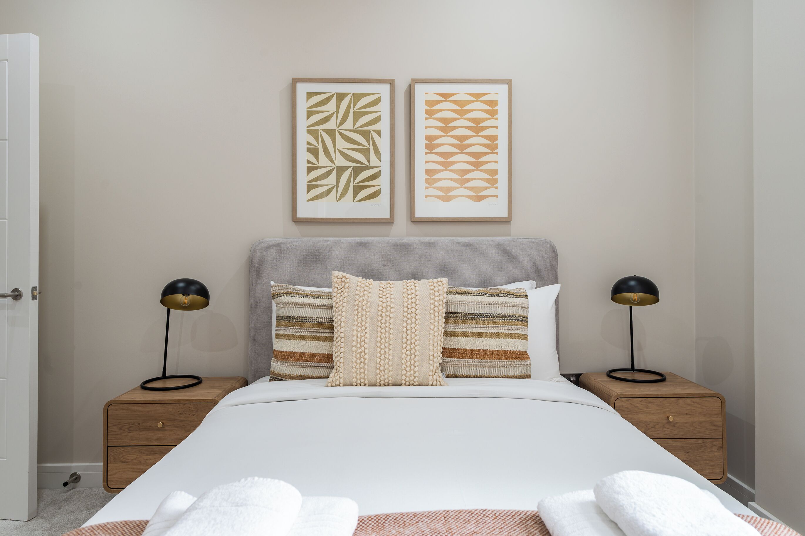 Une chambre à coucher bien rangée, avec un lit, deux tables de chevet, une commode et deux lampes fixées au mur.