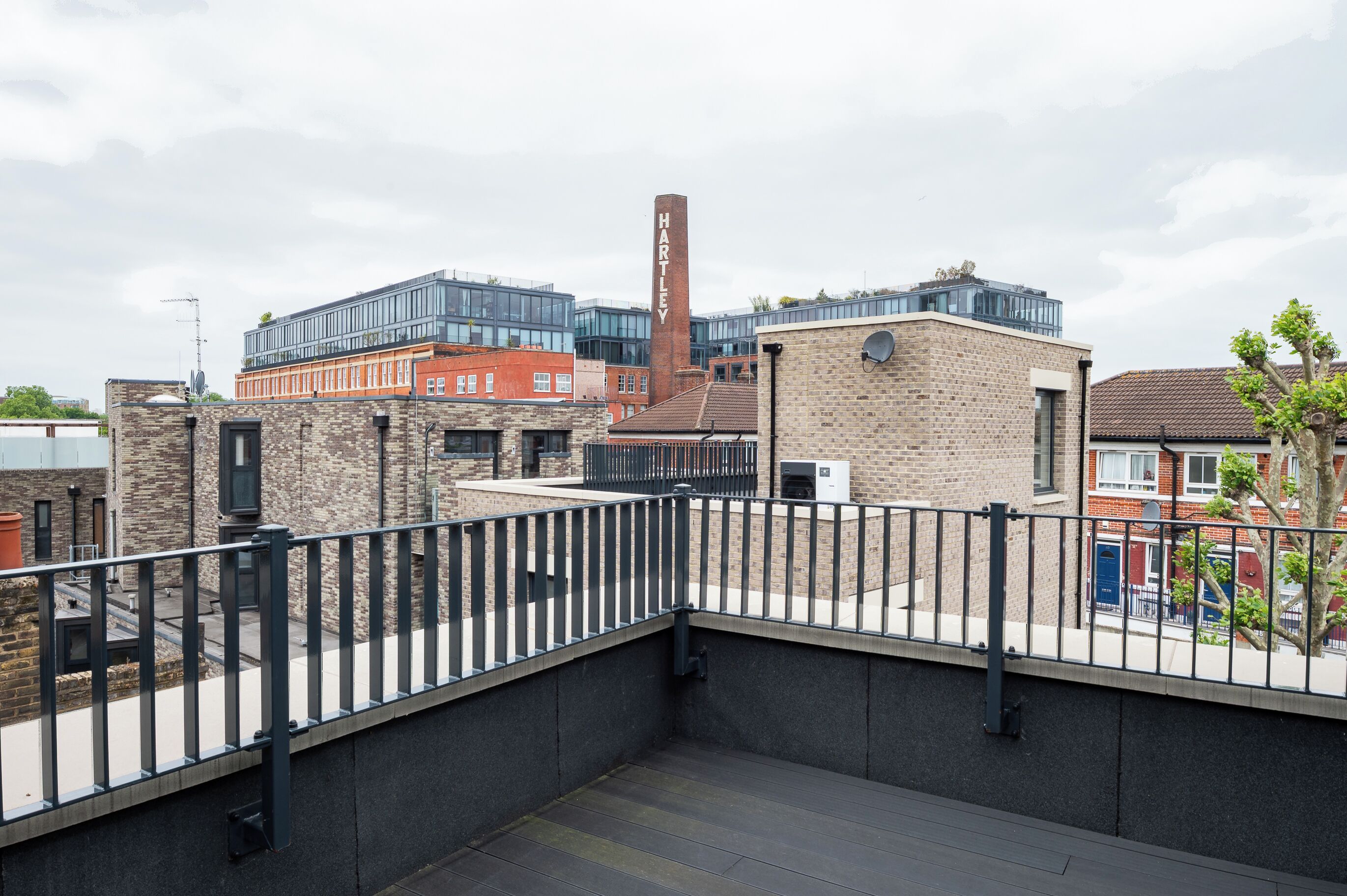 A rooftop terrace with a metal railing, a brick building, and a modern glass structure in the background.