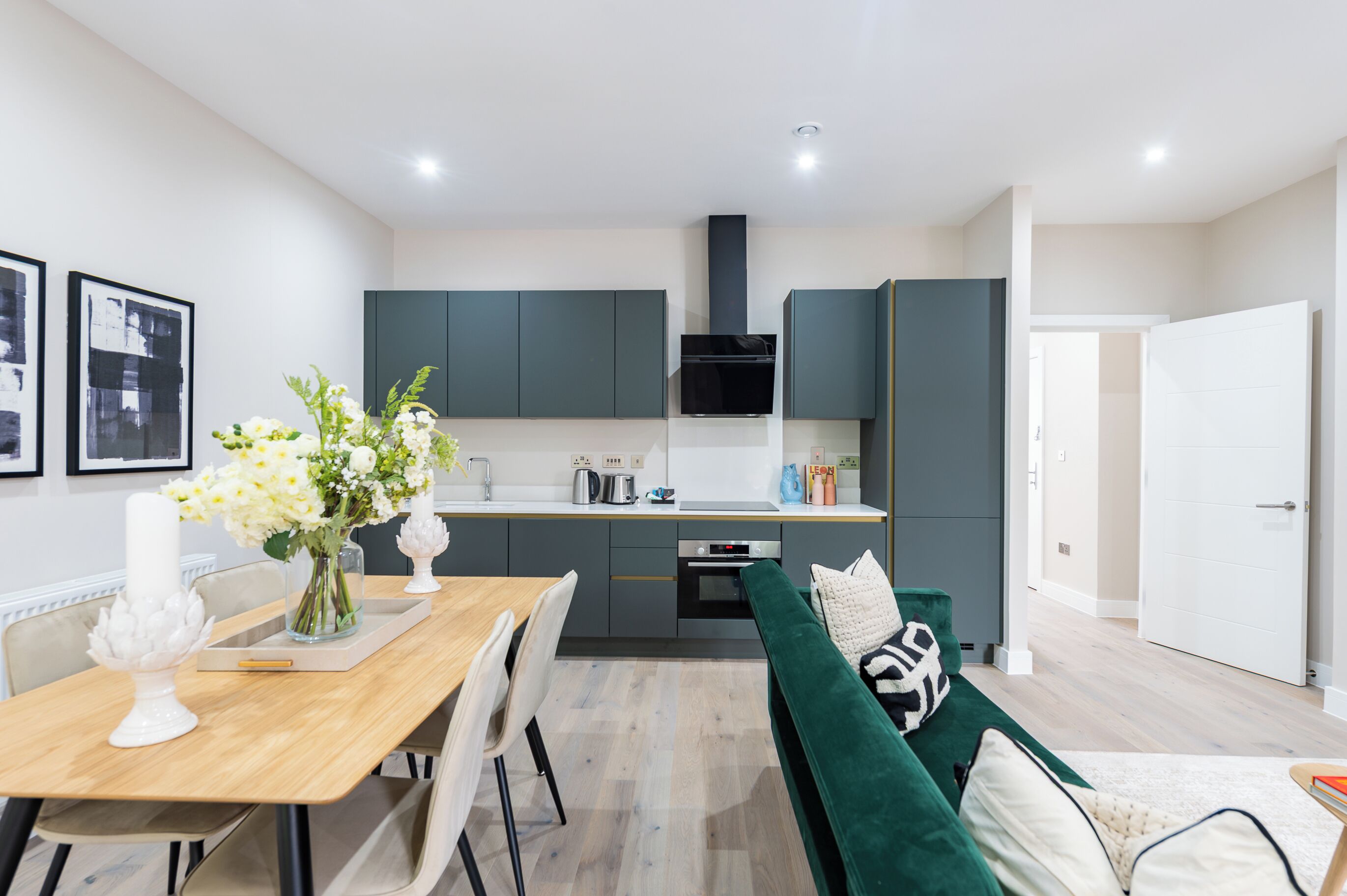 A modern kitchen with dark cabinets, a wooden dining table, and a green sofa.