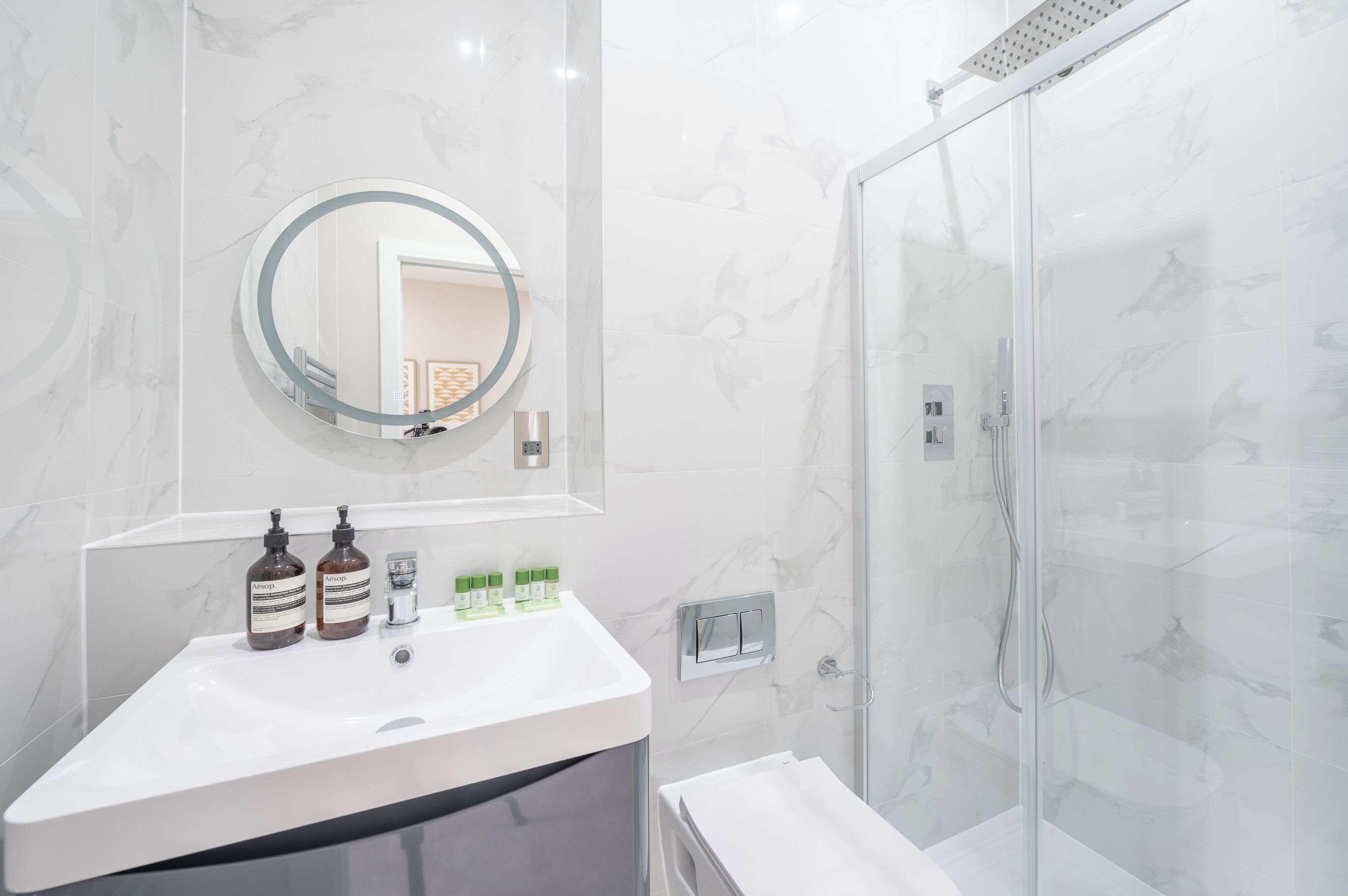 A modern bathroom with a white sink, a round mirror, and a glass shower enclosure.