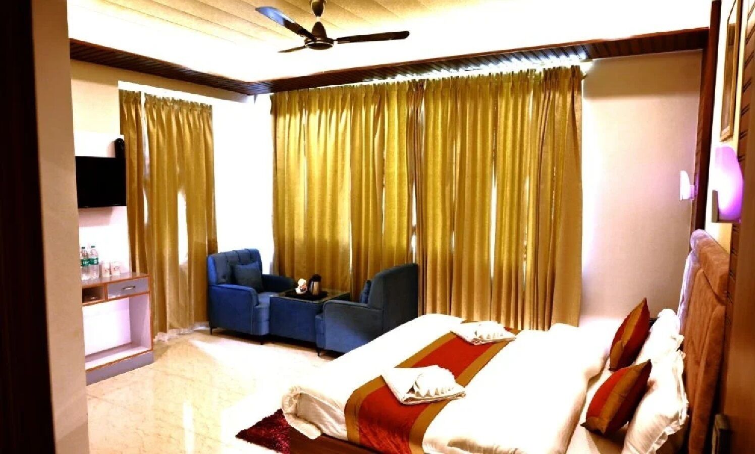 A hotel room with a bed, a sofa, a TV, and curtains.