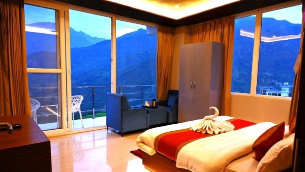 A hotel room with a large bed, a wardrobe, a desk, and a balcony with a view of mountains. - R Narayan Pleasant Inn Hotel - Guptkashi (Ukhimath)