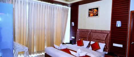 A hotel room with a large bed, a ceiling fan, a wooden headboard, a bedside table, a nightstand, a chair, and a window with curtains.