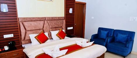 A hotel room with a large bed, a blue sofa, wooden paneling on the walls, and a framed picture on the wall.