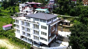 A multi-story hotel with balconies, a rooftop terrace, and a view of surrounding greenery. - R Narayan Pleasant Inn Hotel - Guptkashi (Ukhimath)