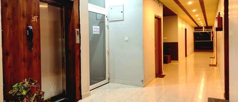 A hotel corridor with a wooden door, a glass door, and a fire extinguisher on the wall.