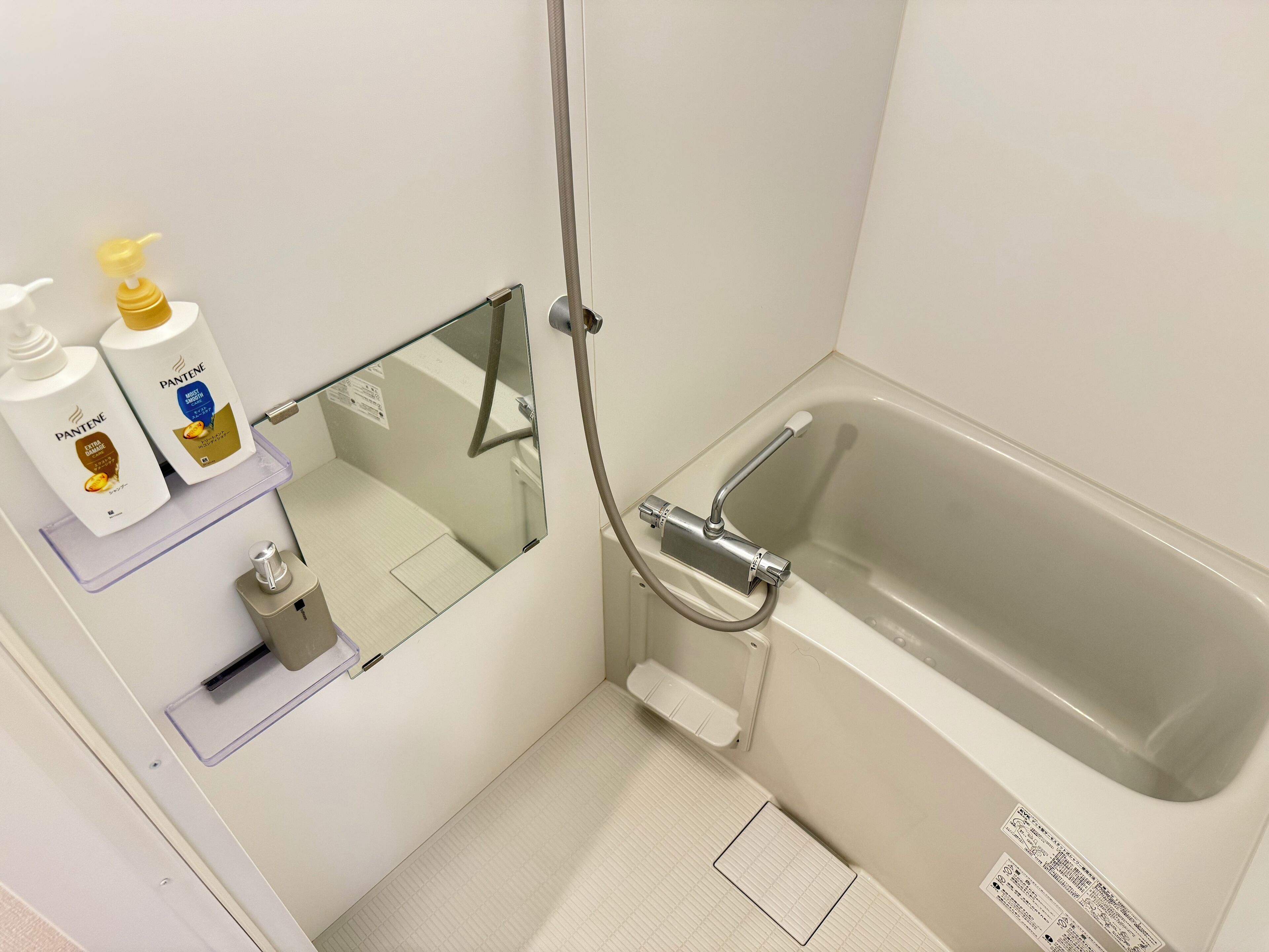 Un baño con bañera, ducha y dos botellas de Pantene en un estante.