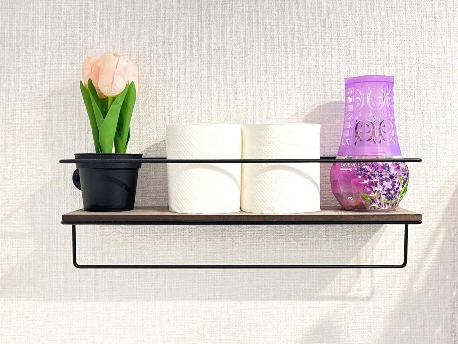 A shelf with a potted plant, toilet paper rolls, and a decorative vase.