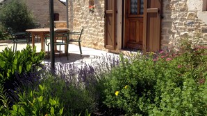 Un edificio de piedra con puerta de madera, una mesa con sillas y un jardín con diversas plantas.