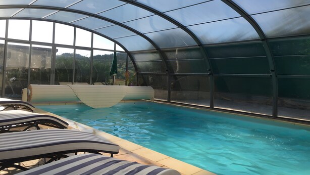Una piscina interior con paredes de vidrio transparente, sillones de descanso y vistas del paisaje circundante.