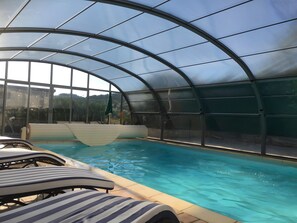 Una piscina interior con paredes de vidrio transparente, sillones de descanso y vistas del paisaje circundante.