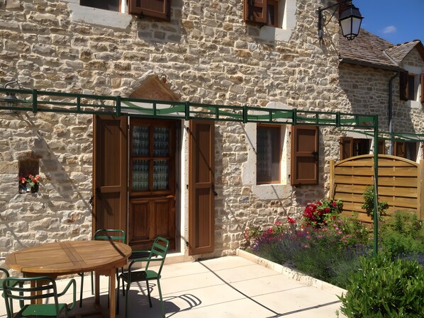 Un edificio de piedra con puerta de madera, una ventana pequeña y una pérgola de metal verde.