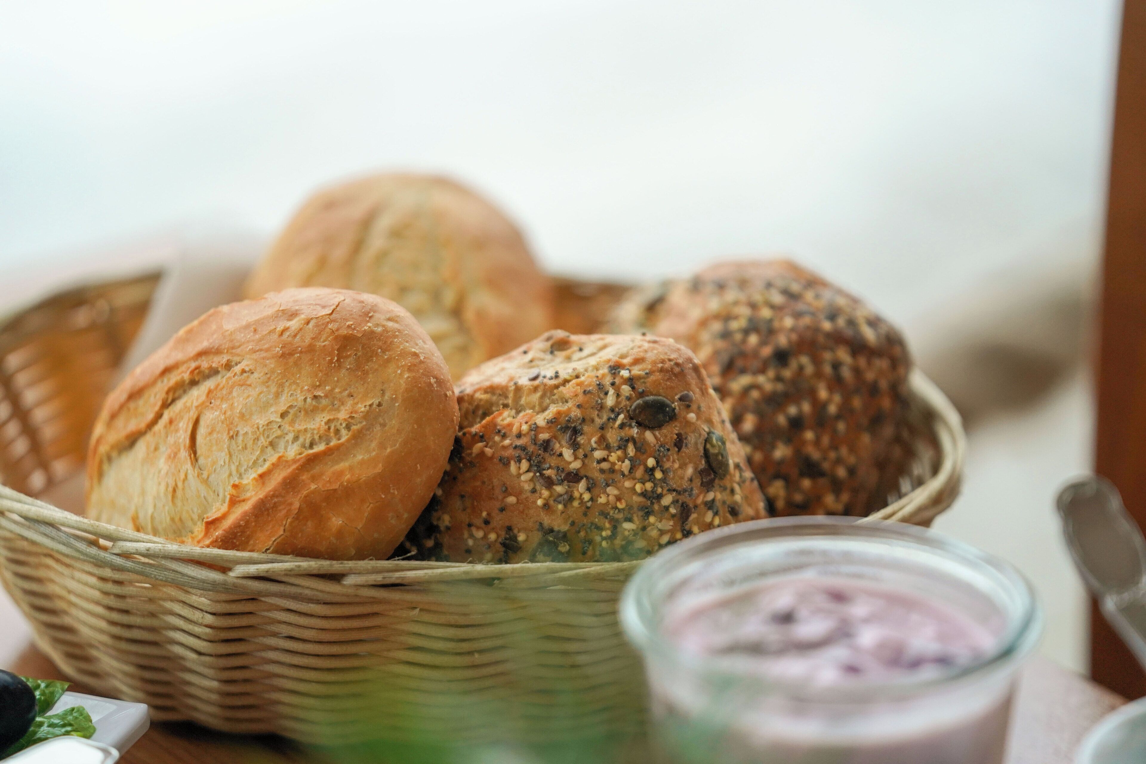 Een mand met verschillende broden, waaronder volkoren en zadenbrood, op een houten tafel.
